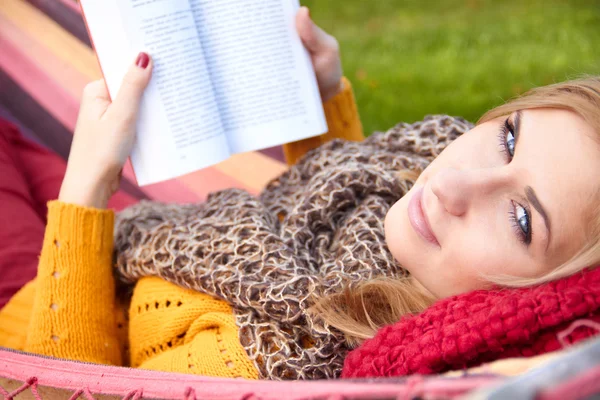 Jovem descansando em uma rede e lendo um livro — Fotografia de Stock