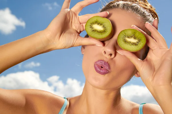 Happy young woman holding kiwi in front of her eyes over sky bac — Stock Photo, Image
