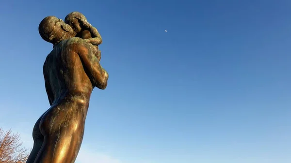 Ostersund, Sweden, March 11, 2022. The bronze statue of a man holding a child towards the afternoon moon. — Stock Photo, Image