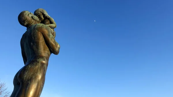 Ostersund, Suecia, 11 de marzo de 2022. La estatua de bronce de un hombre sosteniendo a un niño hacia la luna de la tarde. — Foto de Stock