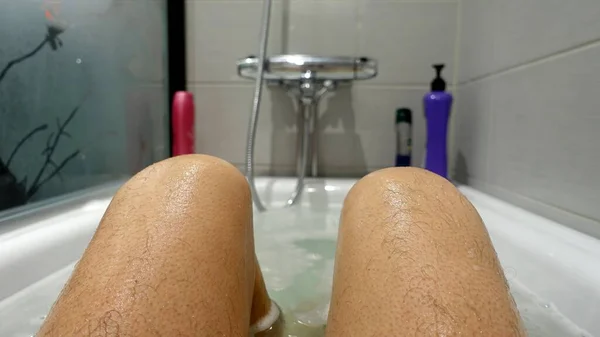 Benen en knieën die tijdens een warm bad uit het water en de zeepcapsules steken — Stockfoto