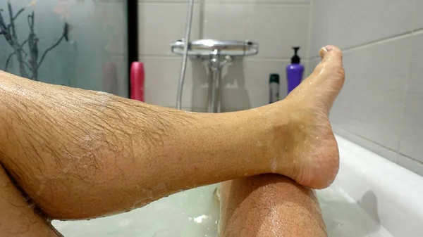 The leg and foot coming out of the water and soap suds during a hot bath — 스톡 사진