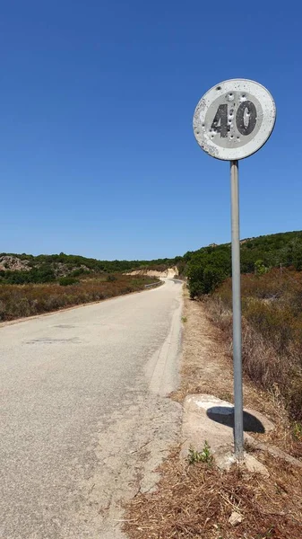 An old road sign on a mountain road indicating the speed limit, perhaps riddled with rifle shots.