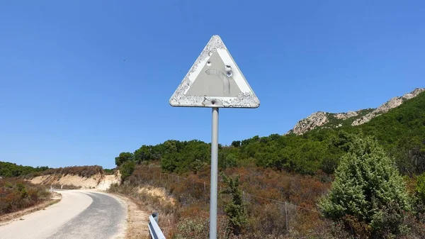 An old road sign on a mountain road indicating a dangerous curve, perhaps riddled with rifle shots.