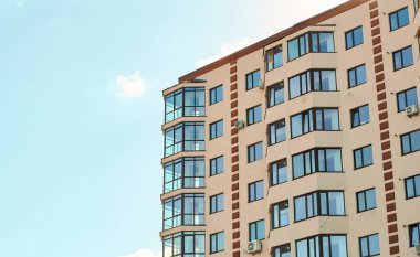 Yeni apartman dairesi tipi. Modern kum sıva cephesi, büyük bir pencere balkonu ve cam pencereleri var. Daireler bloğu. Şehir emlakçılığı. Basit apartman mimarisi