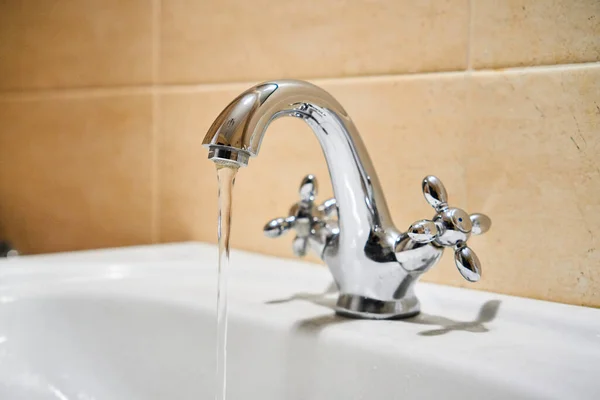 Common mixer tap. Water flowing out of bathroom stainless steel pillar tap into sink. Wasting water by leaving chrome faucet tap running. Overusing household water. Water misuse in domestic duties — Stock Photo, Image