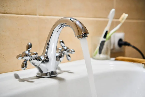 Common mixer tap. Water flowing out of bathroom stainless steel pillar tap into sink. Wasting water by leaving chrome faucet tap running. Overusing household water. Water misuse in domestic duties — Stock Photo, Image