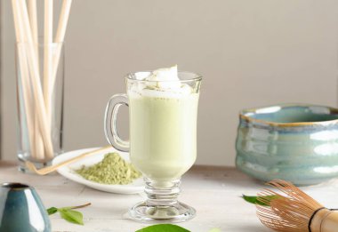 Matcha latte içeceği, bardakta sütlü yeşil çay ve hafif arka planda aksesuarlar..