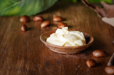 Ahşap bir tabakta rafine edilmemiş Shea yağı, ahşap arka planda fındık ve yapraklar, kapat.