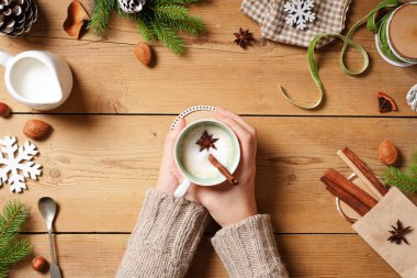 Hint Masala çayı bardağını tutan kadın. Geleneksel Hint içeceği. Süt ve baharatlı, ahşap arka planda Noel temalı dekoratif unsurlar. Boşluğu kopyala, üst görünüm.