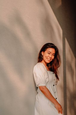 Güzel Asyalı genç kadın gölgeli beyaz duvara karşı.