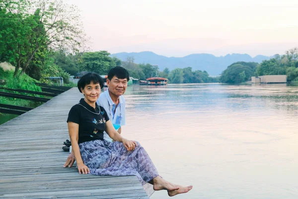 一对亚洲夫妇坐在一条木制的人行道上 看着河上的落日 — 图库照片