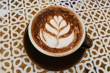 Top view latte art hot chocolate in black ceramic cup on white table.