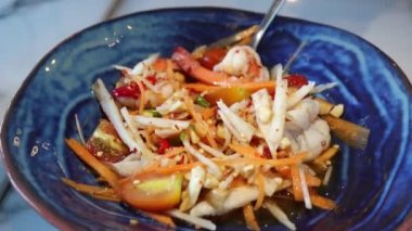 Yeşil papaya salatası Tayland geleneksel mutfak yemekleri. Mavi seramik tabakta baharatlı yeşil papaya salatası..