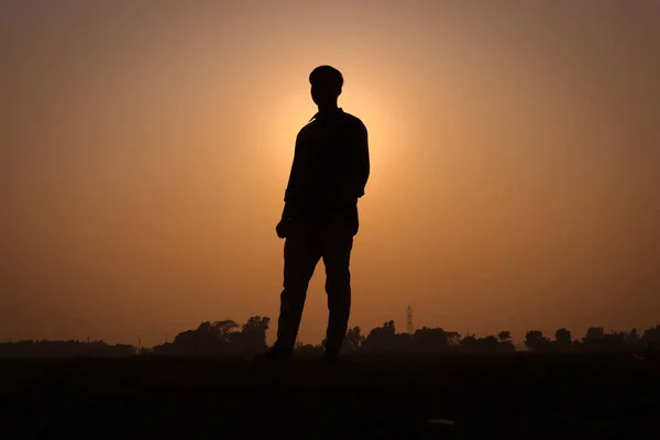 Man silhouette, standing on a rural field and looking straight. Silhouette of a man with a sunset view on a field. Nature concept with a sunset view and a boy standing silhouette close-up photography.