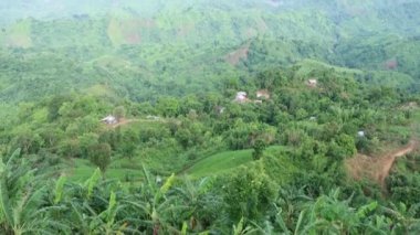 Landscape mountain view with green hilly jungle roads and sky horizon. Aerial drone shot of hilly areas and small houses. Hilly hiking trail 4K footage with large hill area and small residences.