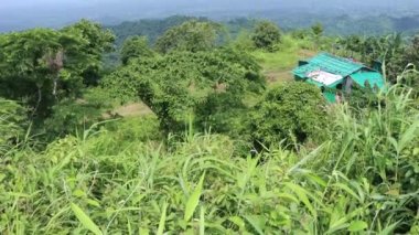 Green hilly area view with small house and cloudy sky. Landscape mountain view with horizon and small hut. 4K footage of a beautiful Hill top aerial view. Hilly jungle area with beautiful horizon view