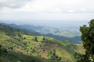 Beautiful hilly landscape area with a cloudy sky. Rural hilly jungle area with green trees and small houses. Aerial landscape mountain drone shot with beautiful sky horizon.