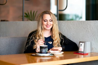 Bir kafede genç bir kadın bir dükkanda kahve içer. Gülümseyen ve kahve karıştıran mutlu bir kadın..