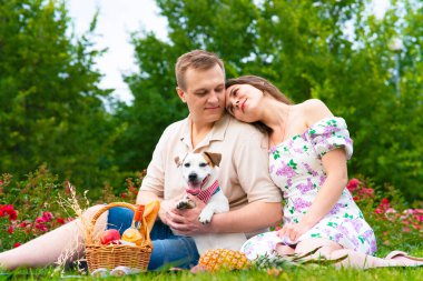 Mutlu bir aile, bahçede piknik yapan genç bir çift. Sevgili kadın ve erkek, köpekleri Jack Russell Terrier ile çimlerin üzerinde.