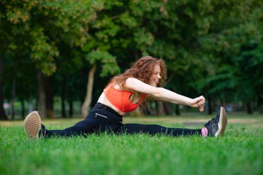 Genç Happy, çimlerin üzerinde gerinen bir kadın. Parkta yaz sporları, sağlıklı yaşam tarzı..