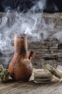 Eski kahverengi buhar bongu ve açık kenevir öğütücüsü ile doğranmış marihuana otu ve tıbbi kenevir tomurcuğu ahşap tüy ve çuval bezi ile duman içinde. Dikey yönelim