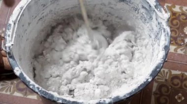 Bir insan, karışımı tamamlamak için çimento ve suyu bir kabın içine karıştırır..