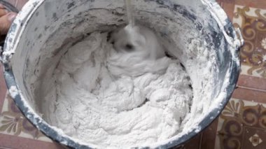 Bir insan, karışımı tamamlamak için çimento ve suyu bir kabın içine karıştırır..