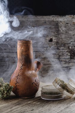 Eski kahverengi buhar bongu ve açık kenevir öğütücüsü ile doğranmış marihuana otu ve tıbbi kenevir tomurcuğu ahşap tüy ve çuval bezi ile duman içinde. Dikey