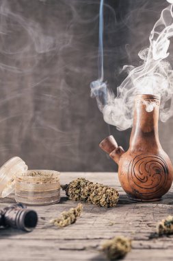 Ahşap yüzeyde tıbbi marihuanayla birlikte tüttüren eski bir balçık nargilesi var.