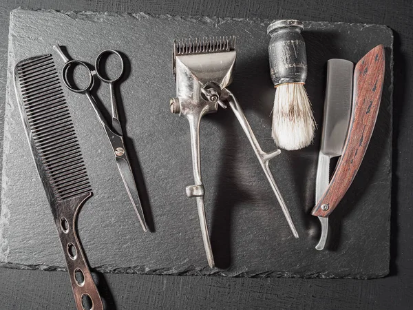 vintage barber tools dangerous razor hairdressing scissors old manual clipper comb shaving brush. on a black slate surface. flat lay top view.