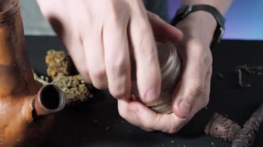 Bir dizi tüten tıbbi esrardan biri. Öğütücüde marihuana öğütmek. Çerçevedeki erkek ellerinde pipo öğütücü tıbbi esrar tomurcukları tüttürüyor. 4k