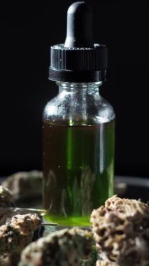 CBD konsantresi olan bir şişe kurutulmuş marihuana tomurcukları ve tıbbi esrarın yanında duruyor. Karanlık arka plan. Ayna masasında dönüyor. 4 bin. dikey video