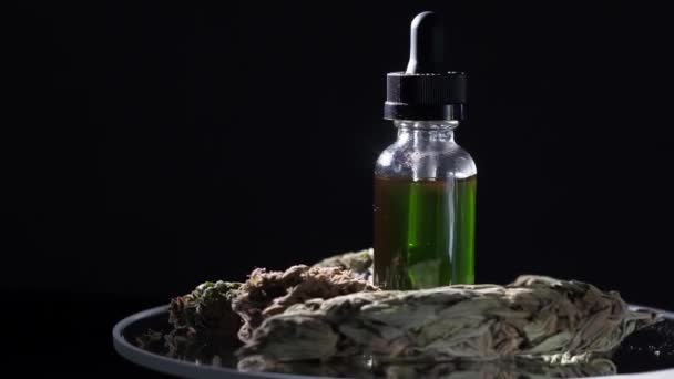 大麻のドロッパーを持つバイアルは 乾燥マリファナ芽と医療大麻の隣に立つCbdを濃縮する 闇の背景 鏡のテーブルの上で回転して — ストック動画