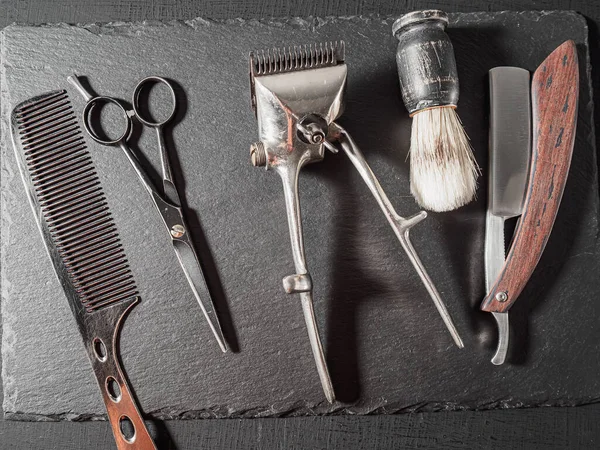 vintage barber tools dangerous razor hairdressing scissors old manual clipper comb shaving brush. on a black slate surface. flat lay top view.