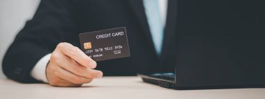 Kredi kartı tutan işadamı, internetten kredi kartı, online ödeme, çevrimiçi alışveriş, e-ticaret, internet bankacılığı, harcama para konsepti gibi şeyleri bilgisayardan satın alıyor..