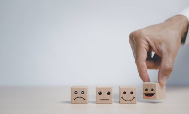 Müşteri hizmetleri değerlendirmesi ve memnuniyet değerlendirme hizmeti değerlendirmesi konseptleri. El, simge yüzlü tahta bloğu seçer, müşteri elini kapatır, gülen yüz simgesini tahta üzerine seçer..