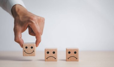 Müşteri hizmetleri değerlendirmesi ve memnuniyet değerlendirme hizmeti değerlendirmesi konseptleri. El, simge yüzlü tahta bloğu seçer, müşteri elini kapatır, gülen yüz simgesini tahta üzerine seçer..