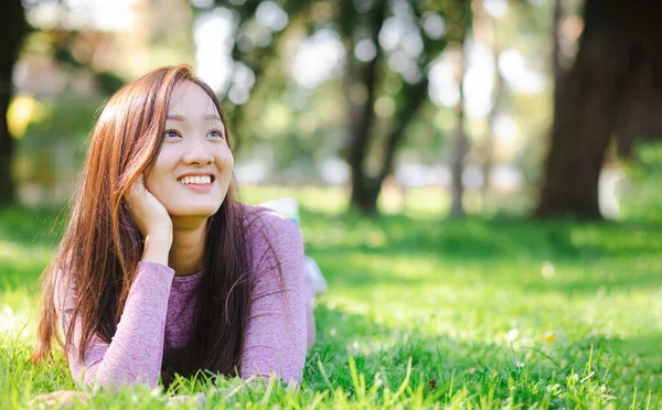 在一个绿色的夏季公园里 身穿运动衫 面带微笑的亚洲年轻漂亮女子躺在绿草上 — 图库照片