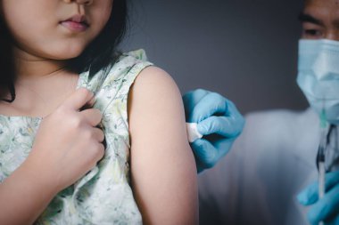 Asyalı doktor çocuk doktoru, sevimli Asyalı kıza aşı enjekte ediyor, küresel bir salgın sırasında çocuk aşısı, doktor kolunun yanında şırınga tutarken başka tarafa bakıyor.,