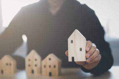 Mini ahşap ev modelini ahşap masadan seçen, emlak almayı planlayan, emlak almayı planlayan bir adam. En iyisini seç konsepti.