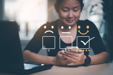 Mutlu ve mutsuz gülen surat konsepti Müşteri Hizmetleri değerlendirme konsepti. Gülümseyen Asyalı kadın akıllı telefon kullanıyor, kadın yüz ifadelerine basıyor sanal dokunmatik ekranda gülümsüyor..