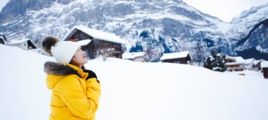 Grindelwald İsviçre 'nin Avrupa tepesinde, sarı paltolu Asyalı bir kadın. Dağlarda tatilde çok mutlu. İsviçre' nin Grindelwald Dağı 'nda karlı bir kış gezisi., 