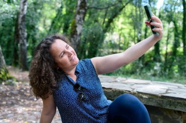 Beyaz bir kadın ormanda piknik yaparken selfie çekiyor..