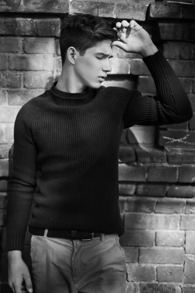 Fashion portrait of young man in black sweater poses over wall — Stock Photo, Image