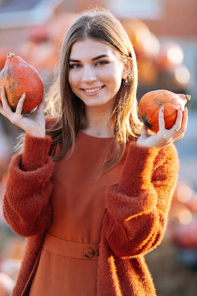 农贸市场上，手握成熟的橙子南瓜，手握橙子南瓜，手握橙子南瓜，穿着棕色毛衣的快乐微笑妇女的画像。温暖的秋天是万圣节，感恩节 免版税图库图片