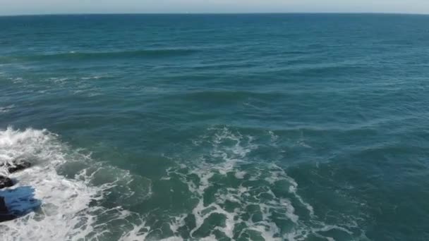 Vista aérea da superfície do mar lambendo ondas para a praia de rocha em dia ensolarado. Textura da superfície da água do oceano, ondas fluidas. Conceito de natureza e turismo — Vídeo de Stock