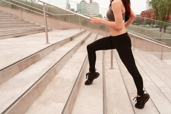 Young dark haired athlete woman running up the stairs while doing cardio in public park. Concept of full life, natural and healthy life. Women\'s sports.