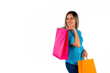 Güzel genç bir kadın, iki elinde renkli alışveriş torbalarıyla, mutlu bir ifadeyle boşluğa bakıyor. Boşluğu kopyala.