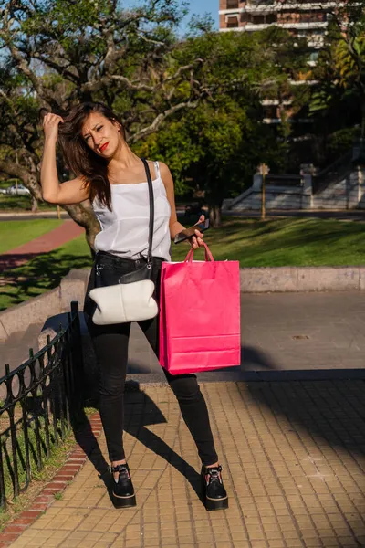 一位美丽的拉丁女人站在人行道上 手里拿着购物袋 手里拿着手机 — 图库照片